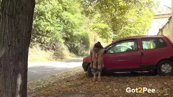 Very daring girl stands and pees next to the road as cars pass by